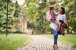 smiling mother holding a daughter with schoolbag in park